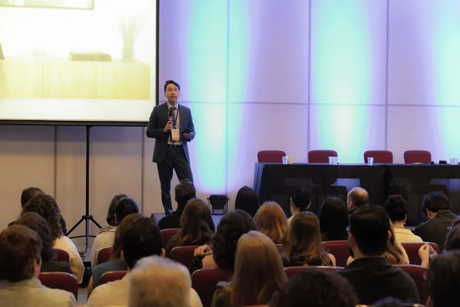 Dr. Ricardo Kobayashi com microfone, apresentando em um auditório
